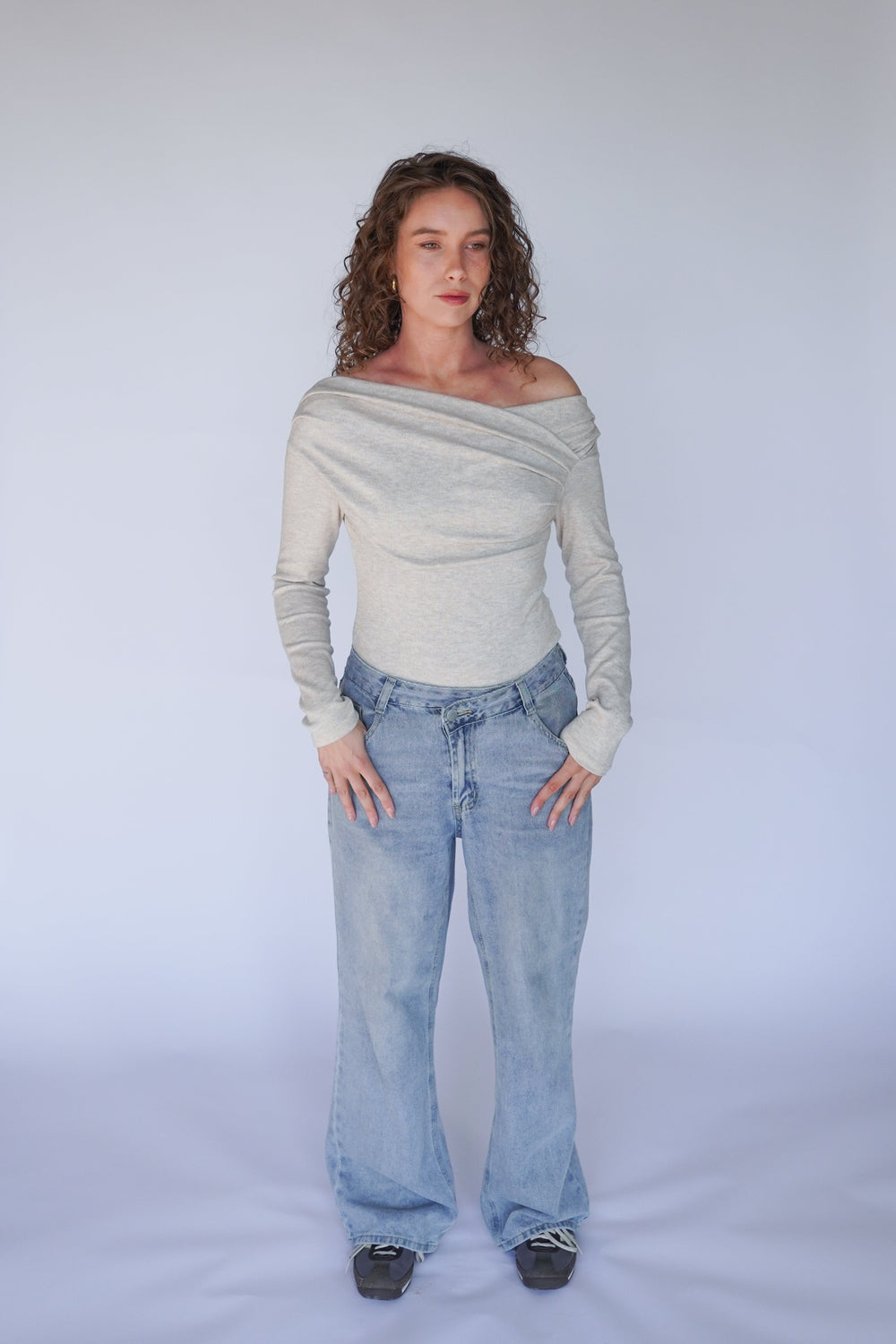 A person wearing light blue denim jeans and a beige off-the-shoulder top with long sleeves.