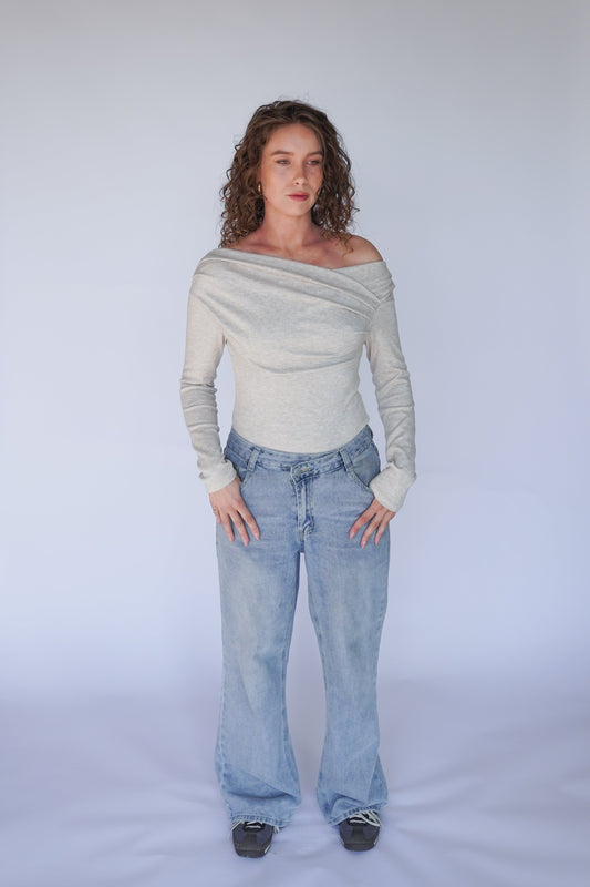 A person wearing light blue denim jeans and a beige off-the-shoulder top with long sleeves.