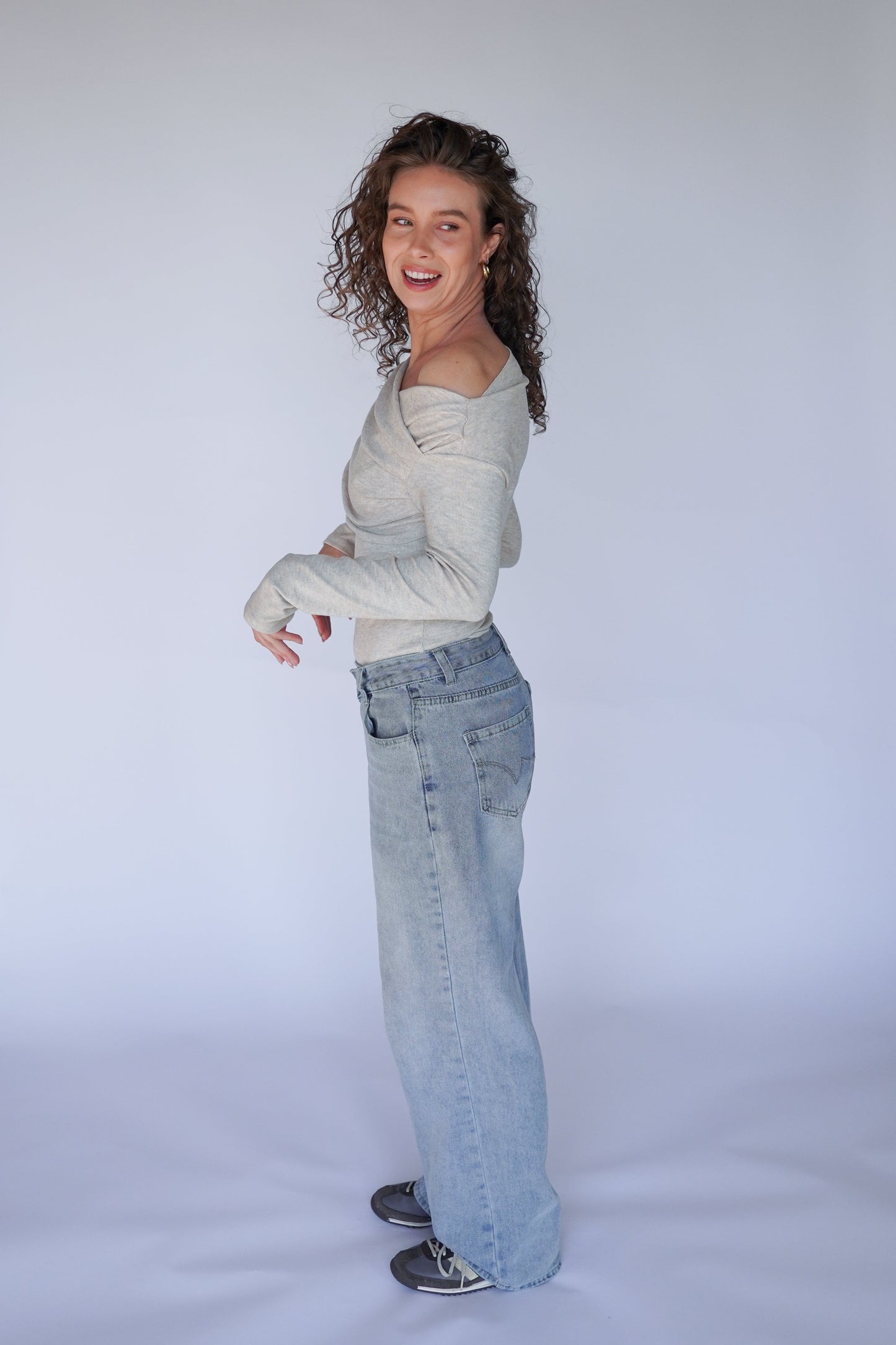 Person wearing a light gray sweater and blue jeans against a white background