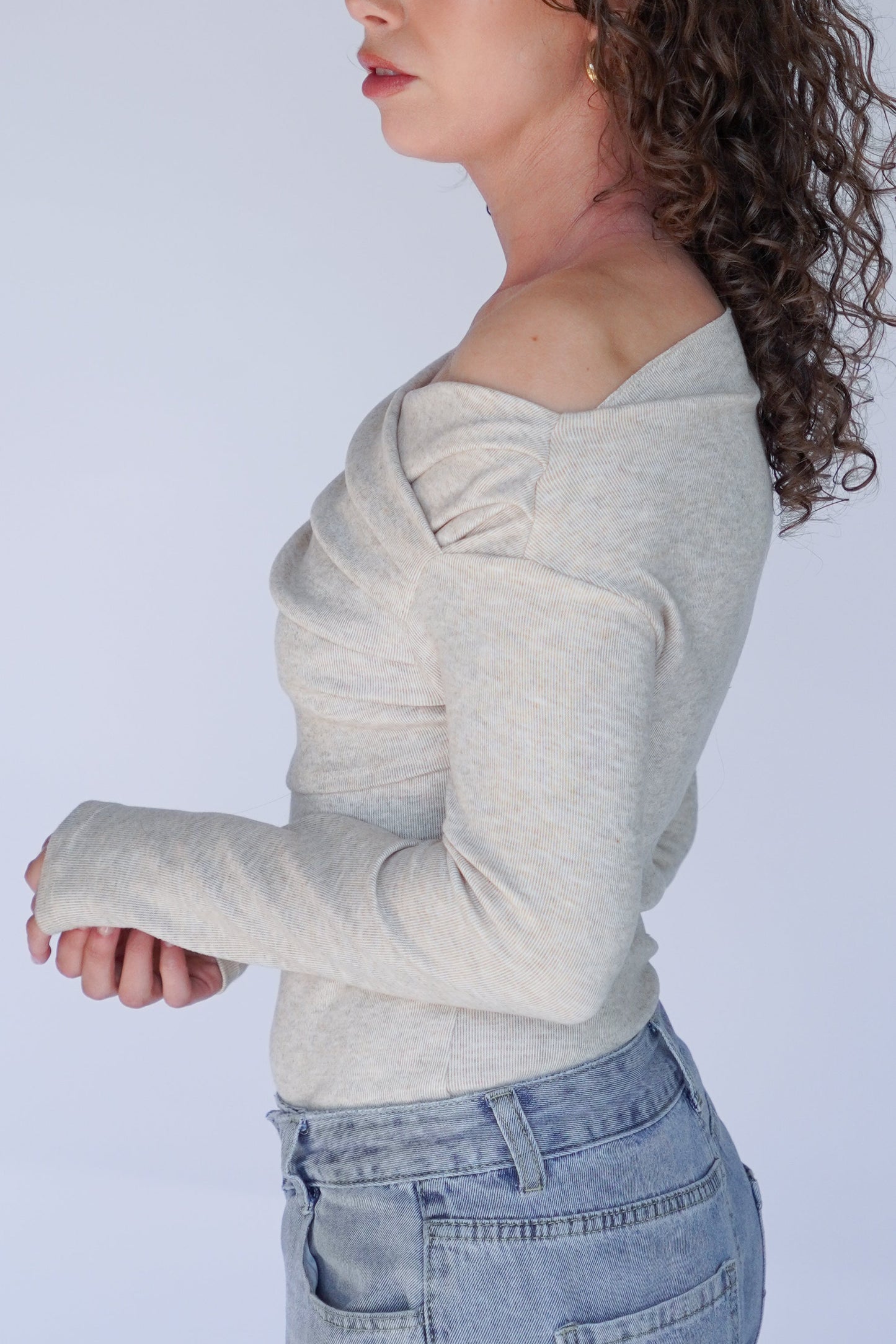 Person wearing a beige long-sleeve top and blue jeans.