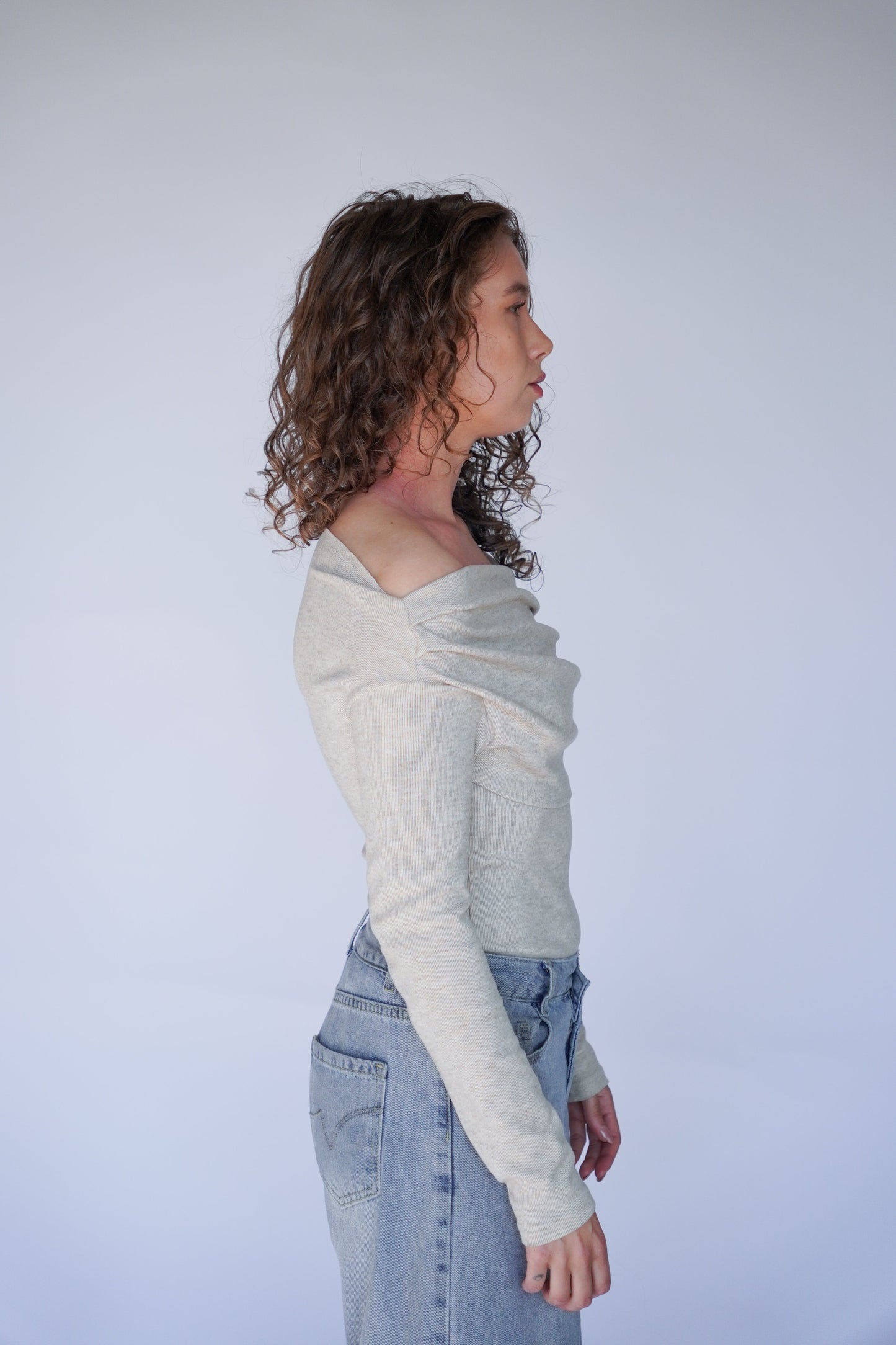 Person wearing a light gray long-sleeve shirt and blue jeans against a plain background.