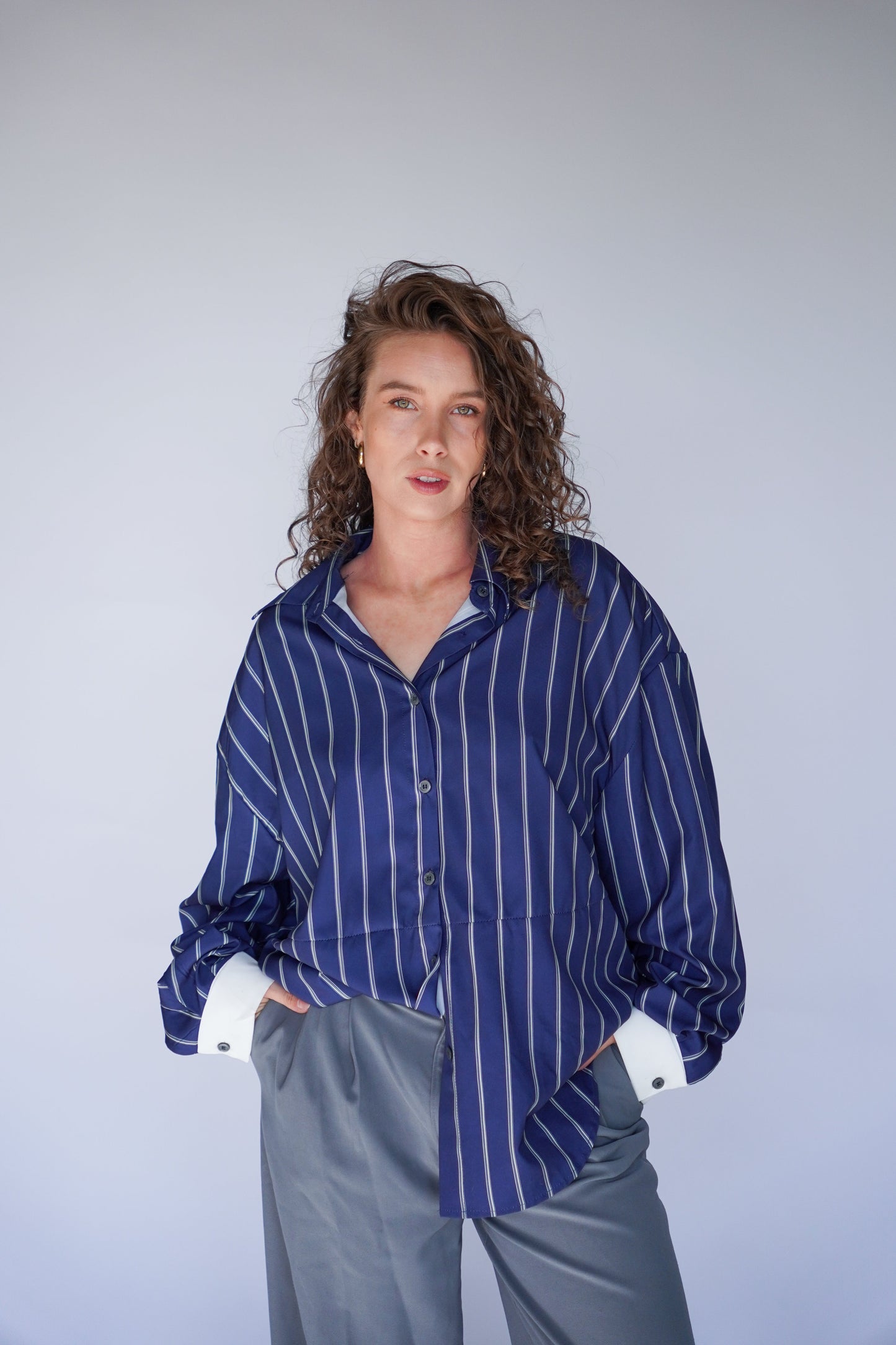 A person wearing a striped blouse in navy and white with long sleeves, paired with light gray trousers.