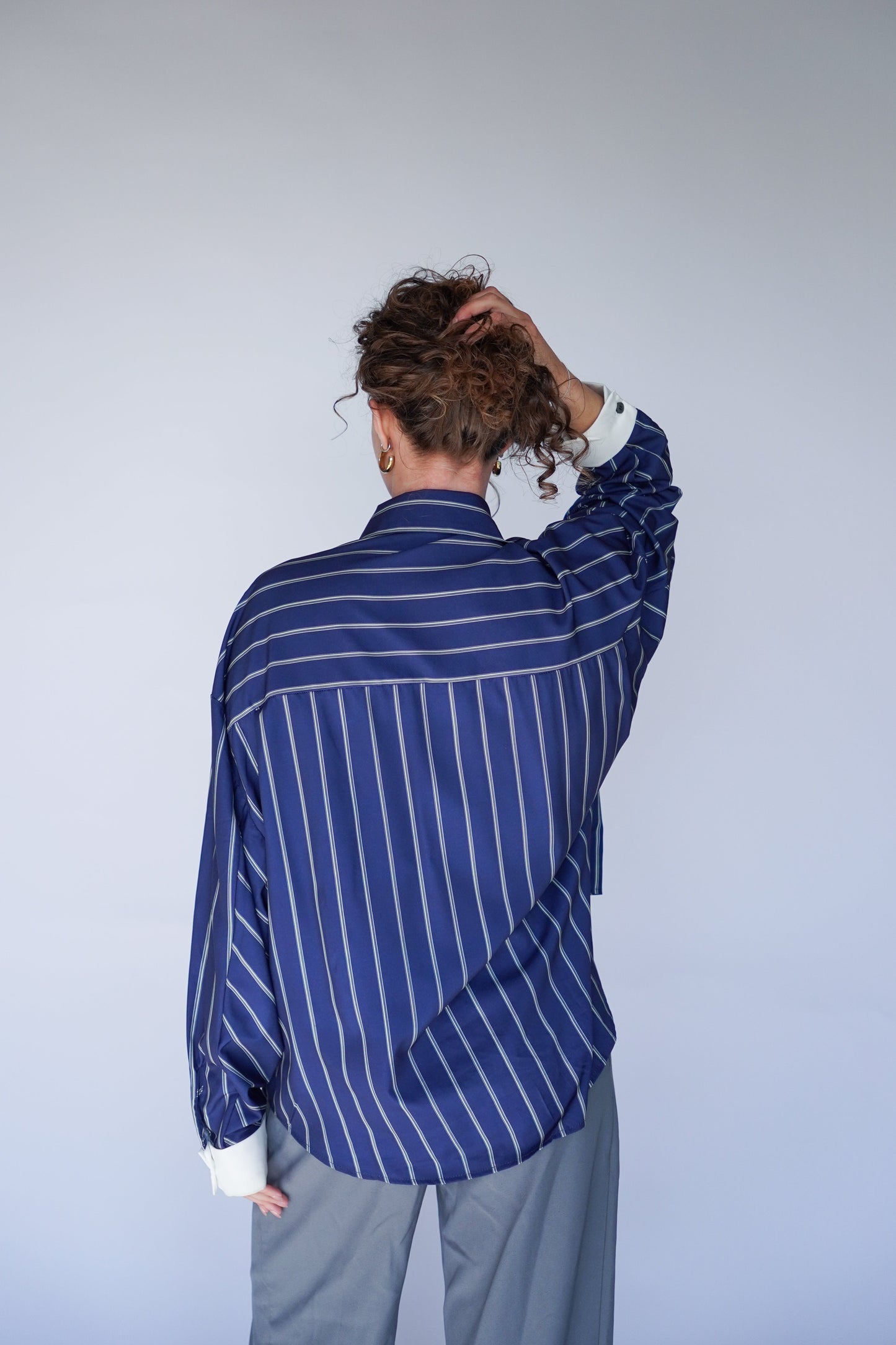 Person wearing a blue striped shirt and gray pants against a plain background