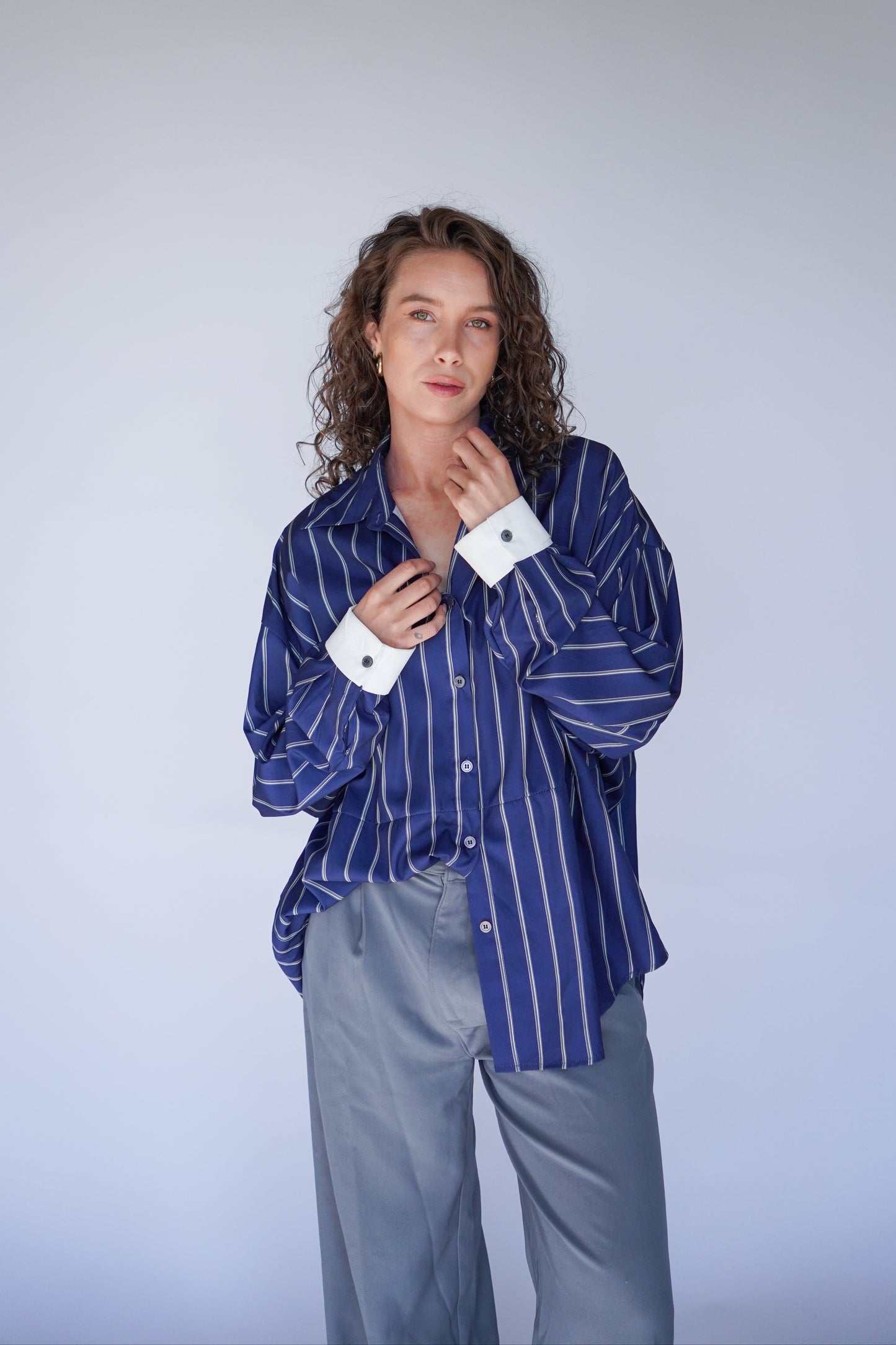 Person wearing a blue striped shirt and light gray pants against a white background