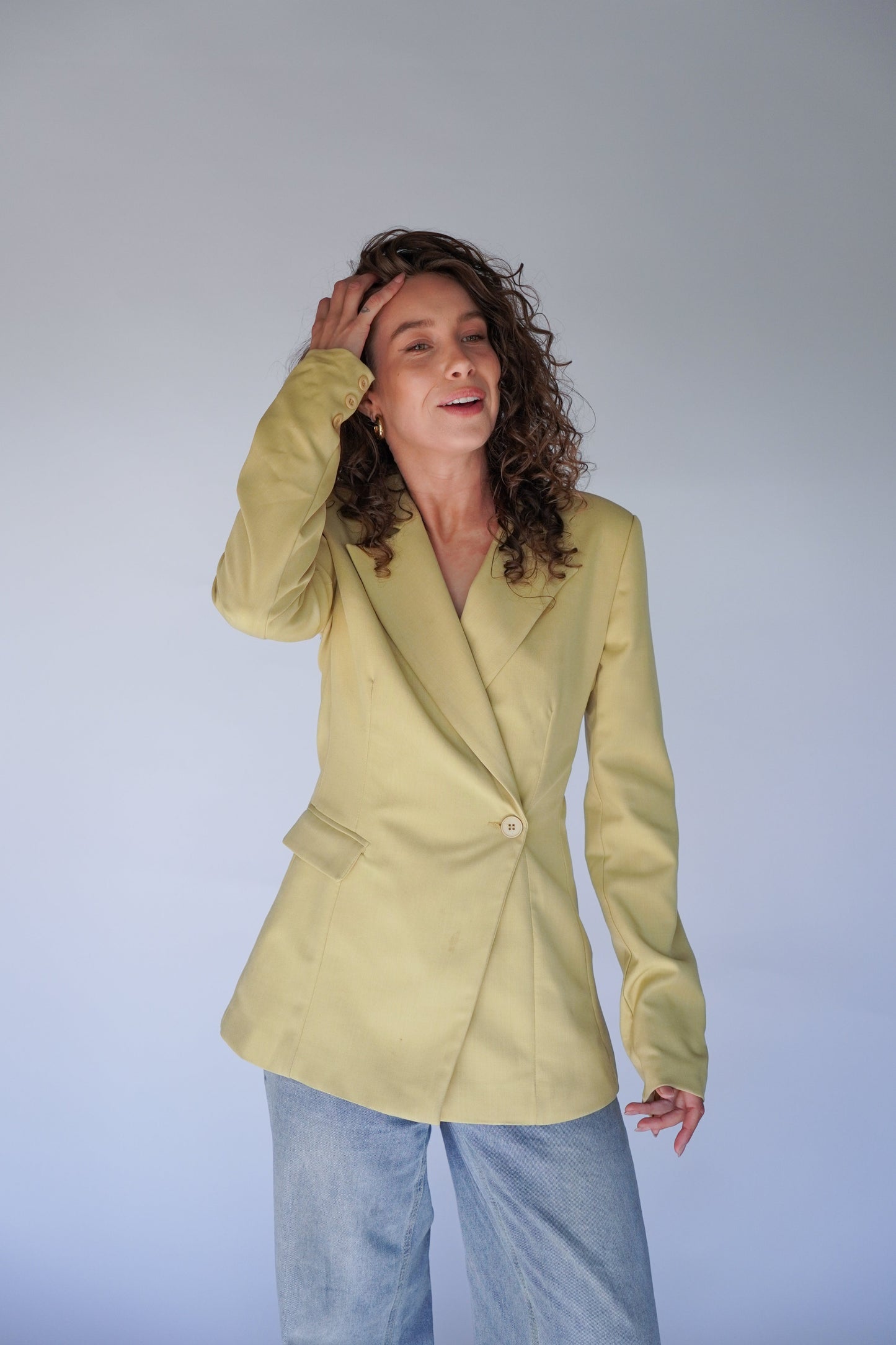 A person posing with a butter yellow blazer over a white top, paired with blue jeans.