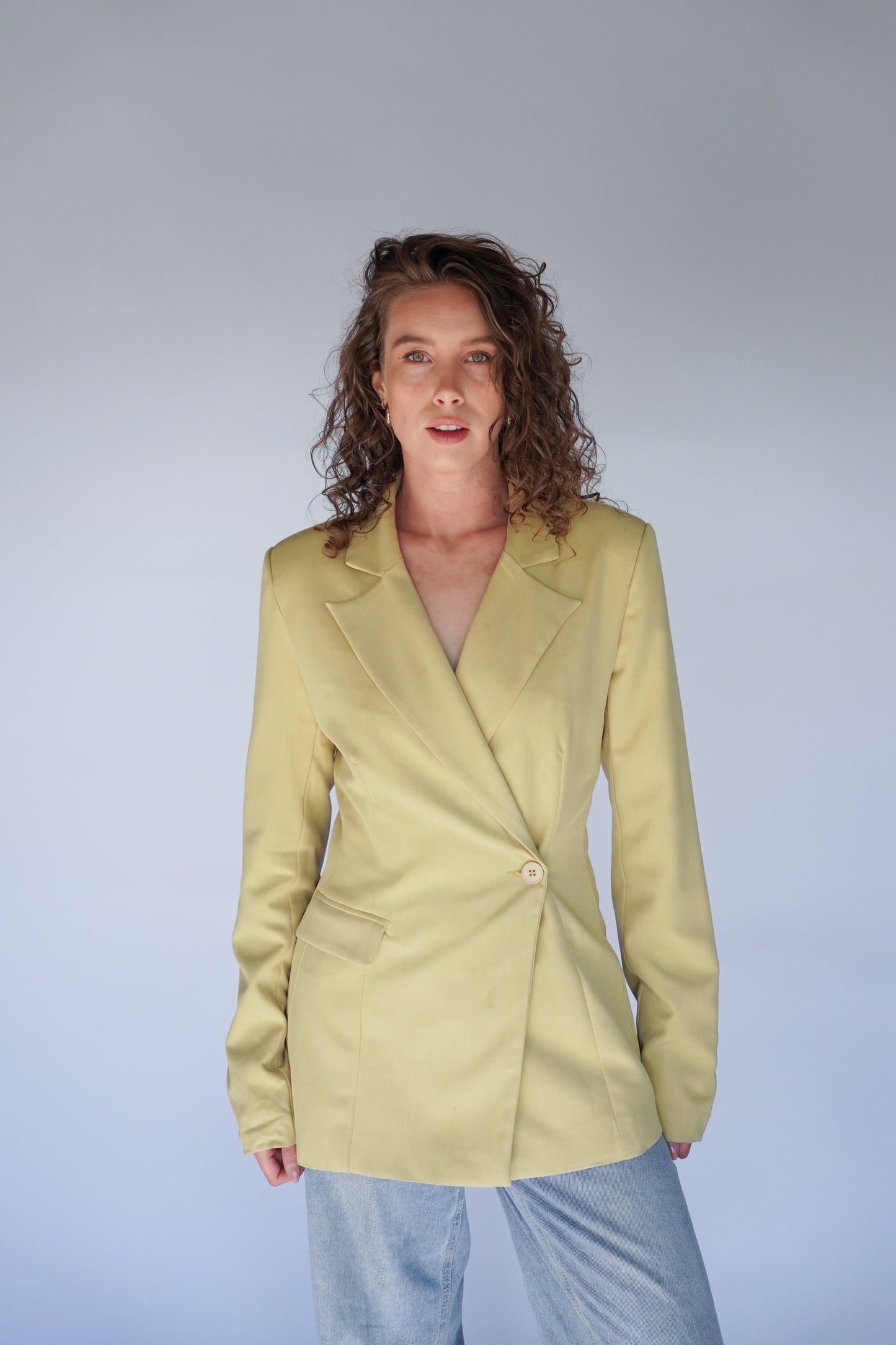 Woman wearing a light yellow blazer against a plain background