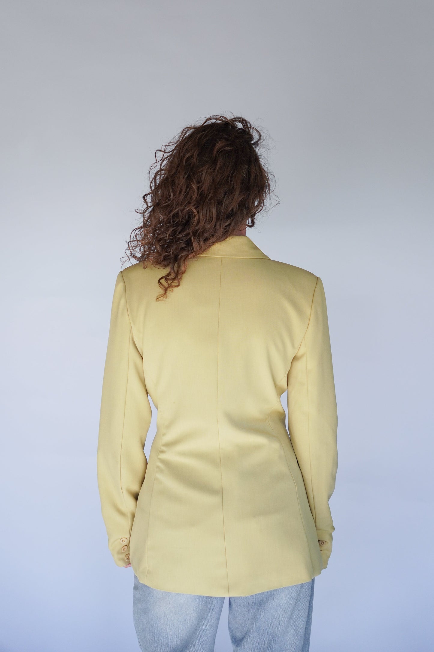 Person wearing a light yellow blazer against a plain background