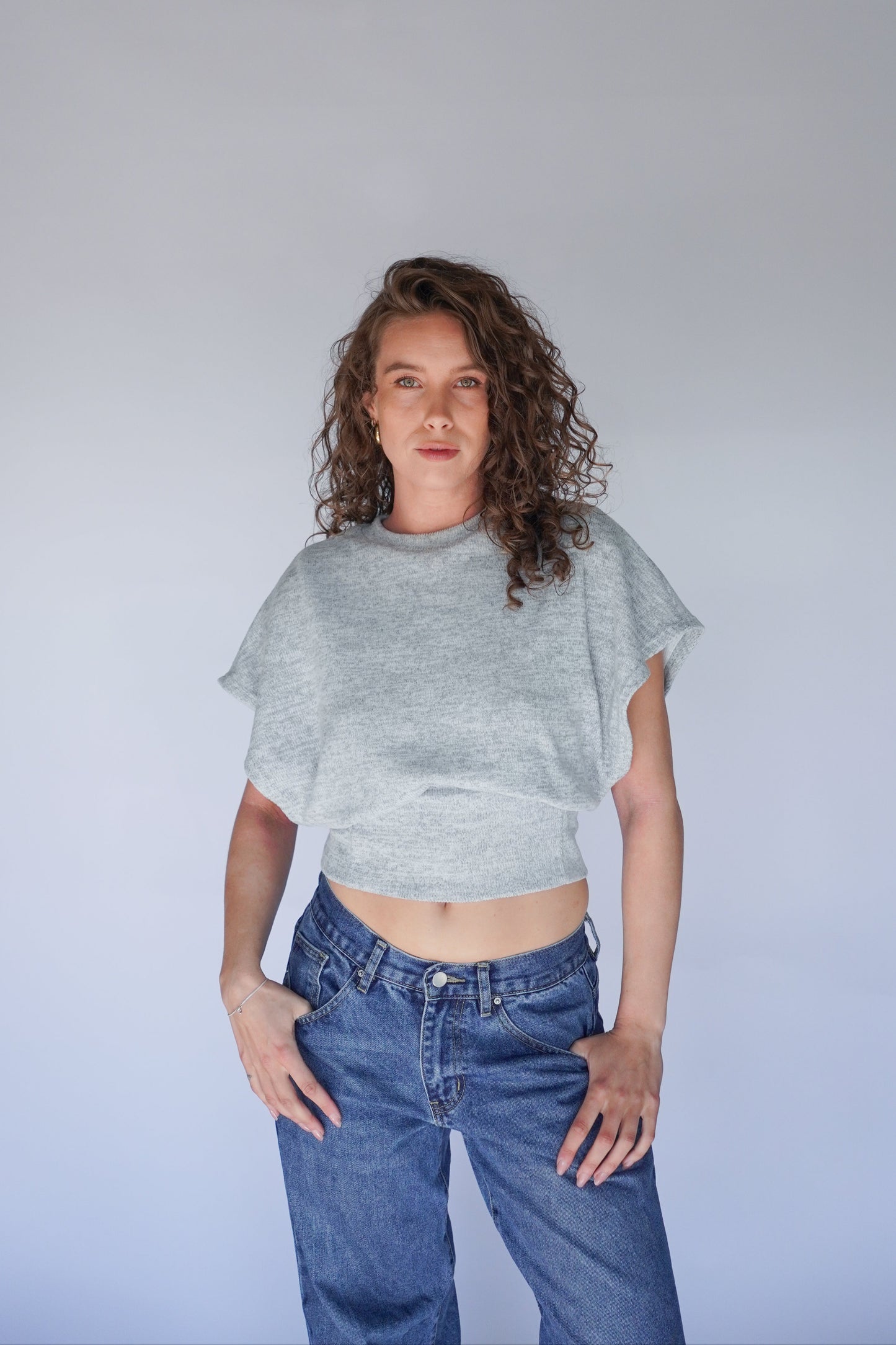 Person wearing a gray crop top and blue jeans against a plain background.