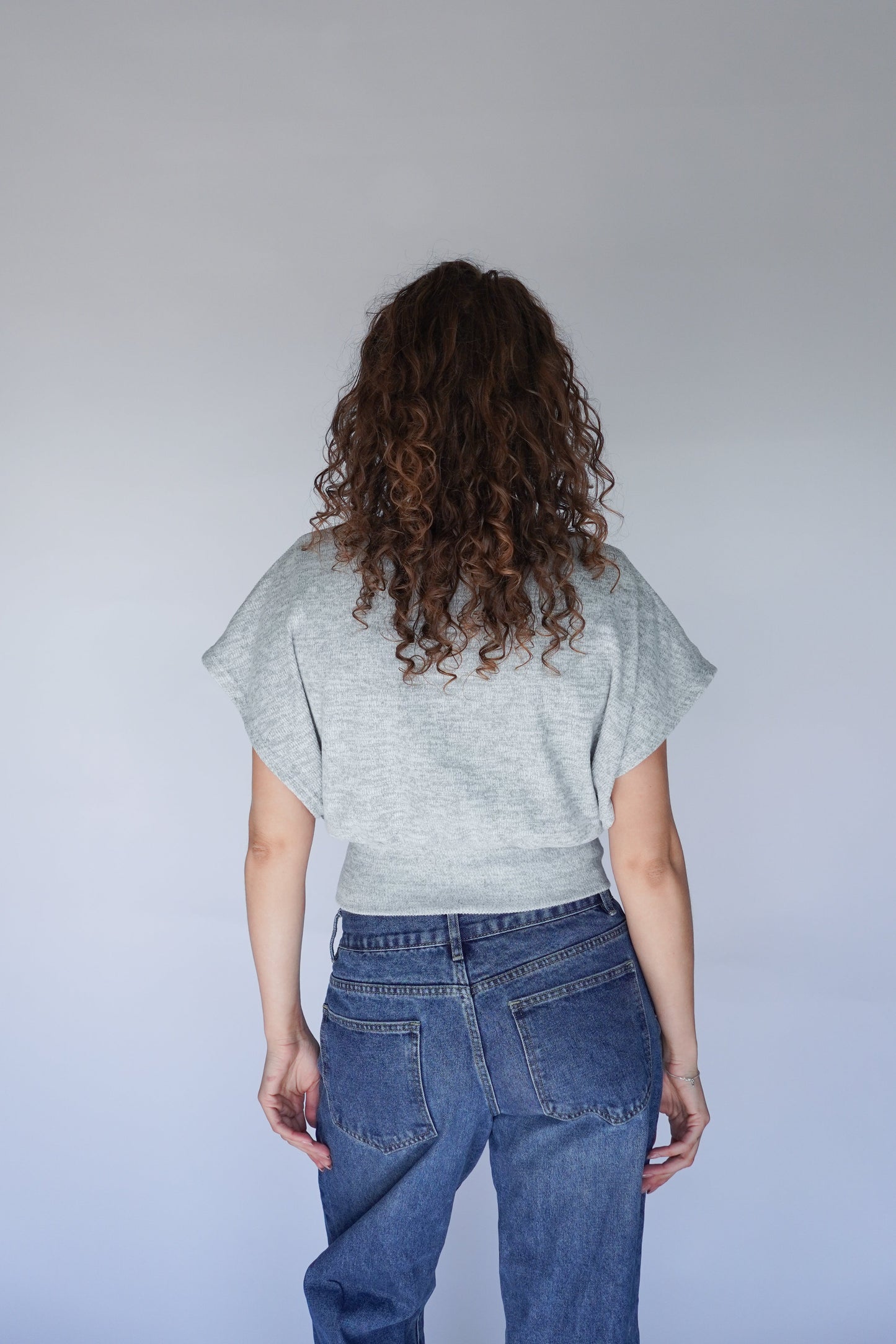 Person wearing a light gray shirt and blue jeans from the back.