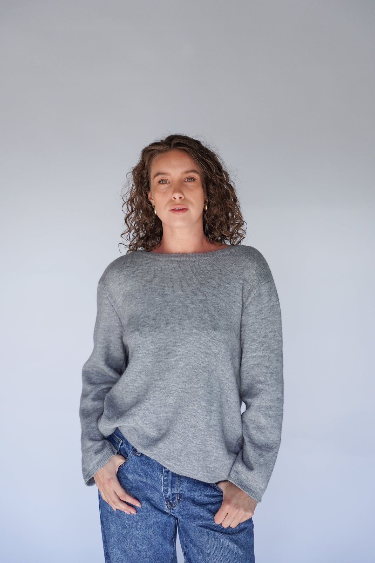 Person wearing a gray sweater and blue jeans against a plain background.