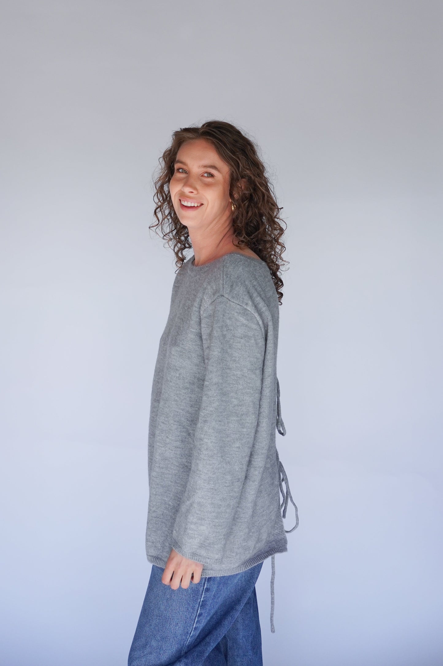 Person wearing a gray long-sleeve shirt and blue jeans against a plain background.