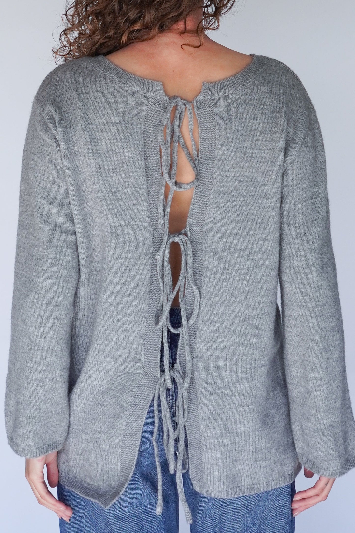 Gray sweater with lace-up back design worn by a person.
