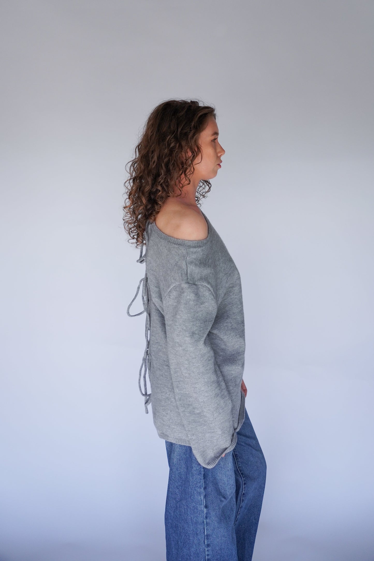 Person wearing a gray sweater and blue jeans against a plain background.