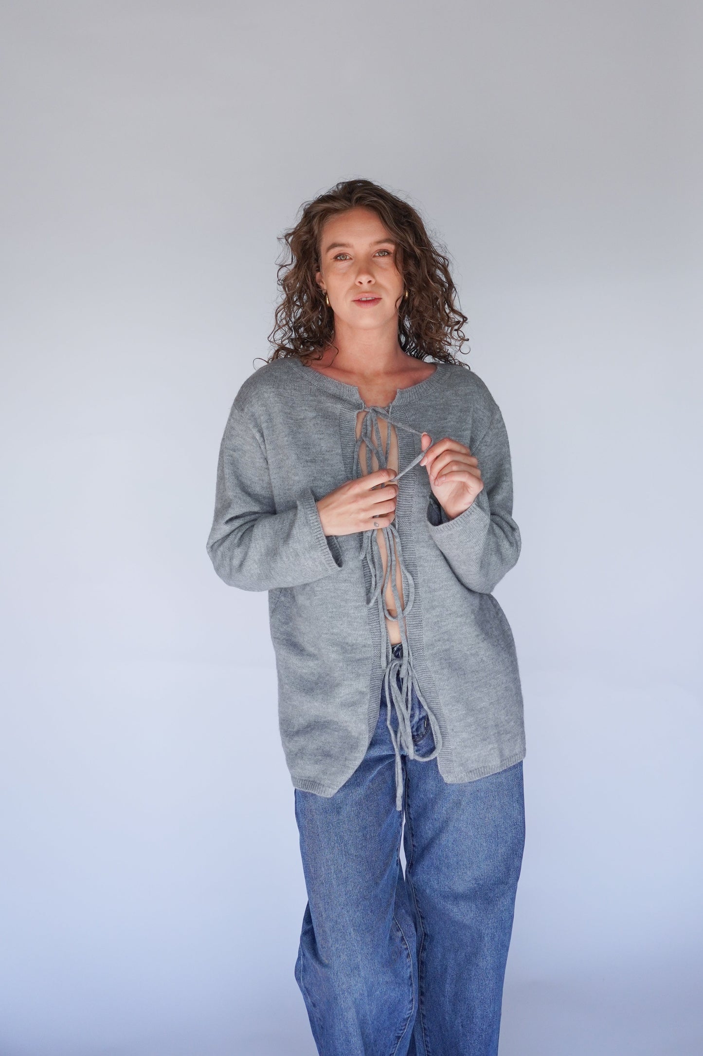 Person wearing a gray cardigan and blue jeans against a plain background