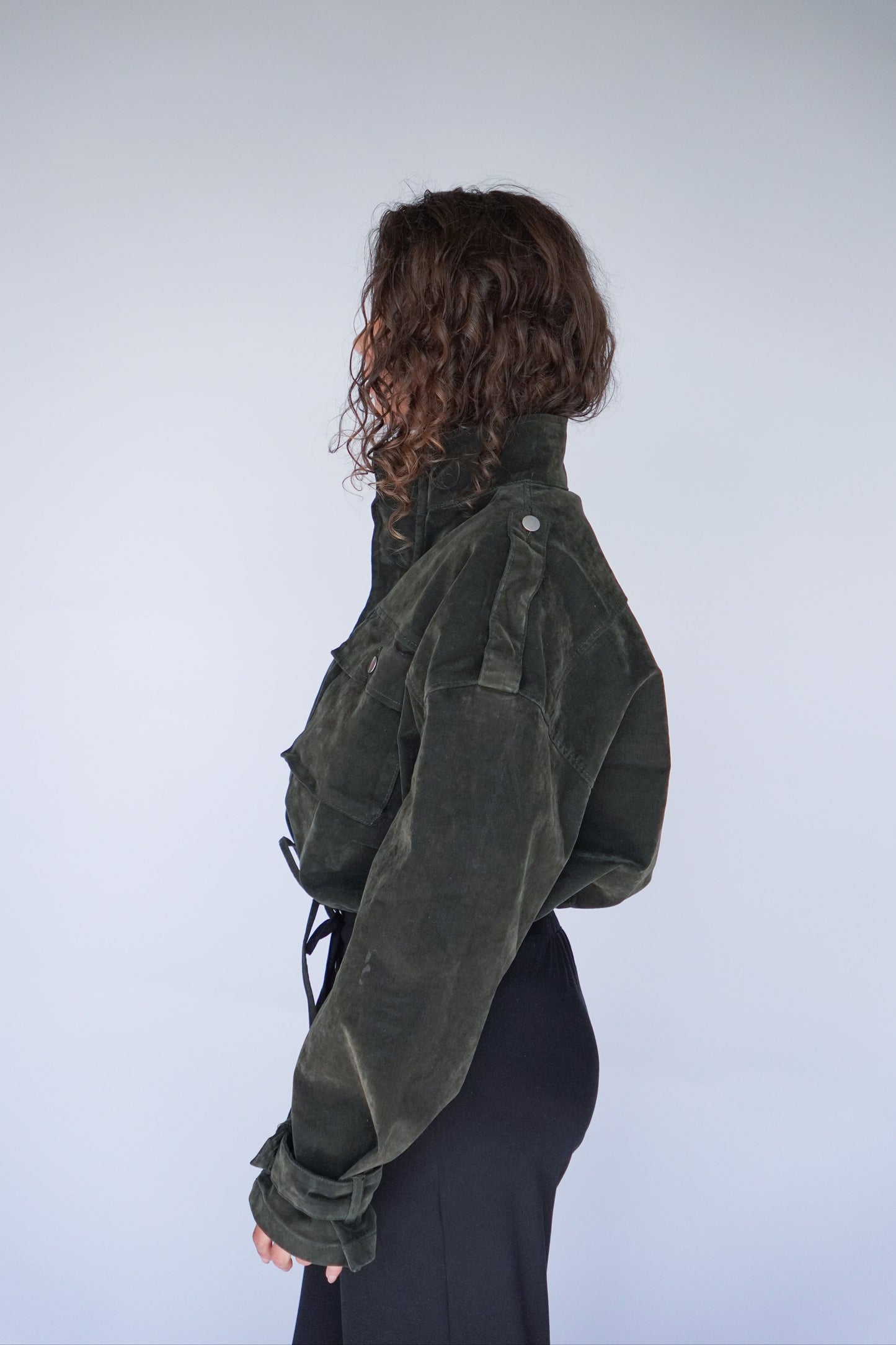 Person wearing a green jacket with their back to the camera on a plain background.