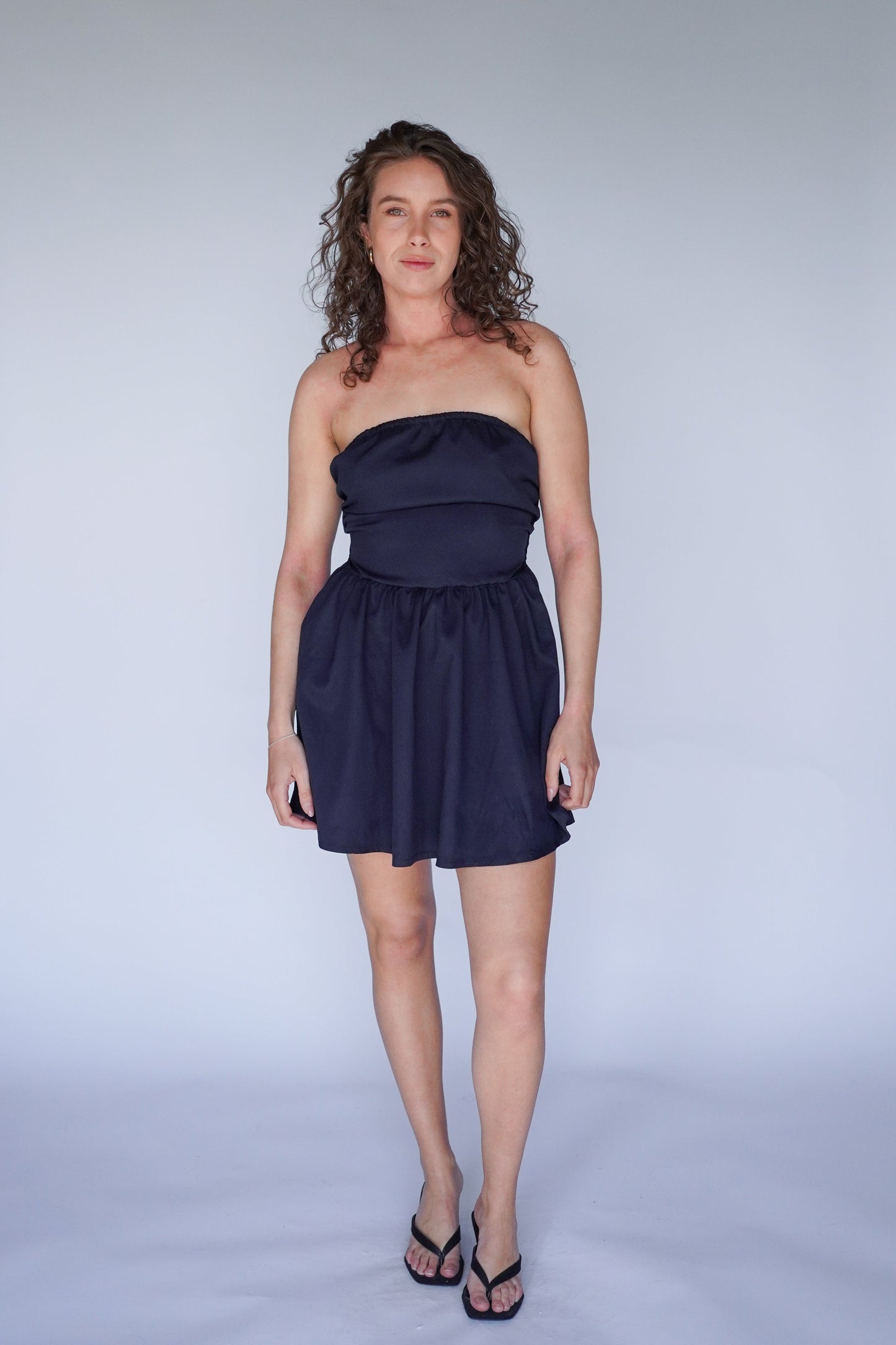 Woman wearing a navy blue strapless dress on a plain background