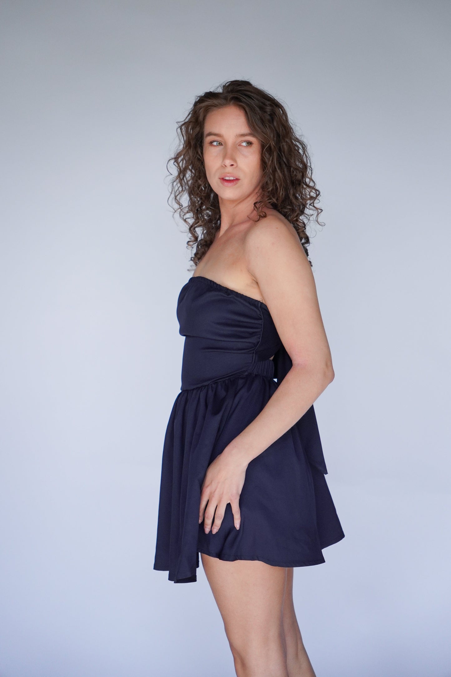 Woman in a dark blue strapless dress against a plain background