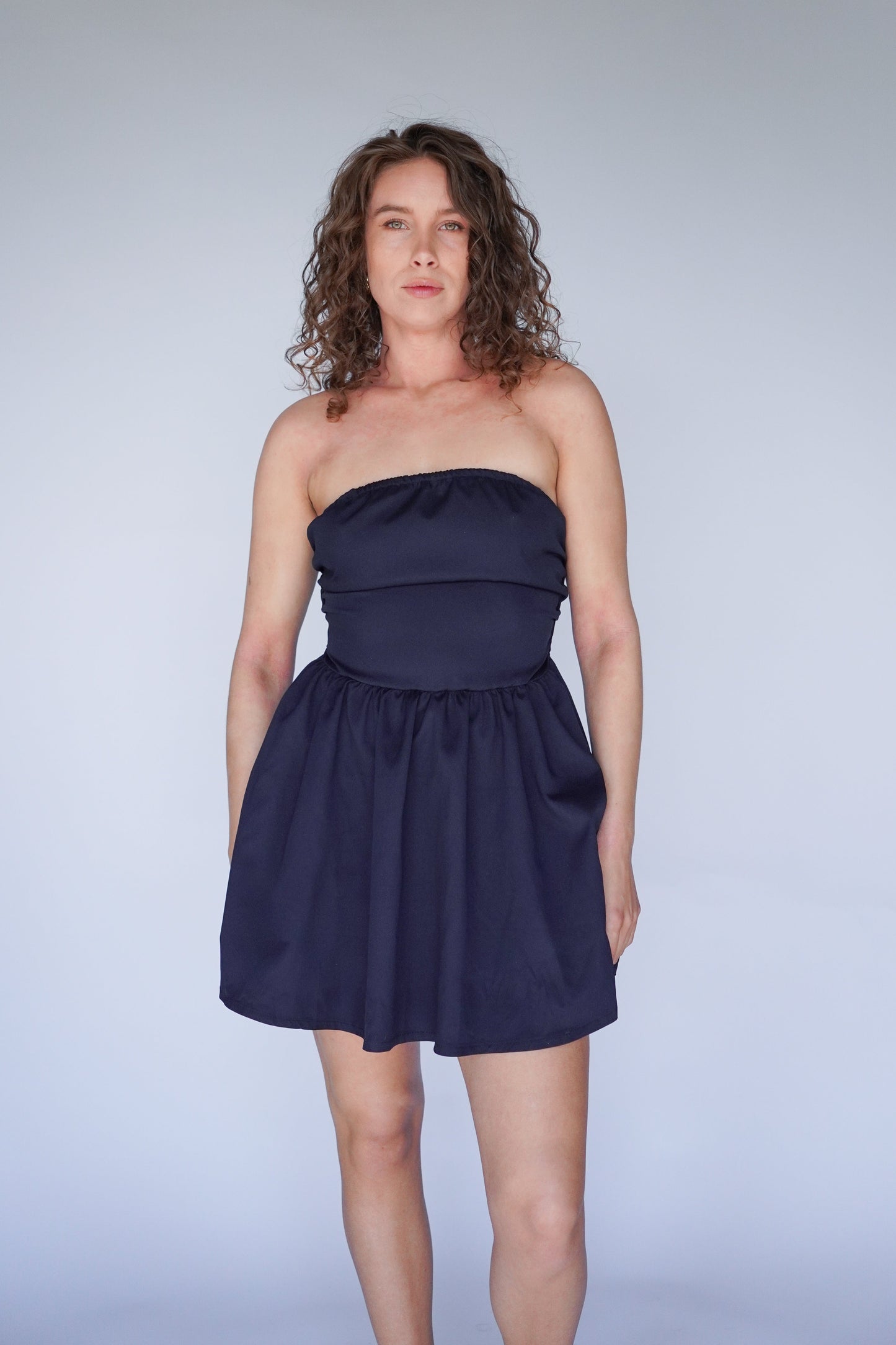 Woman wearing a navy blue strapless dress on a plain background