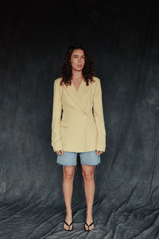 Woman wearing a beige blazer and denim shorts against a dark background