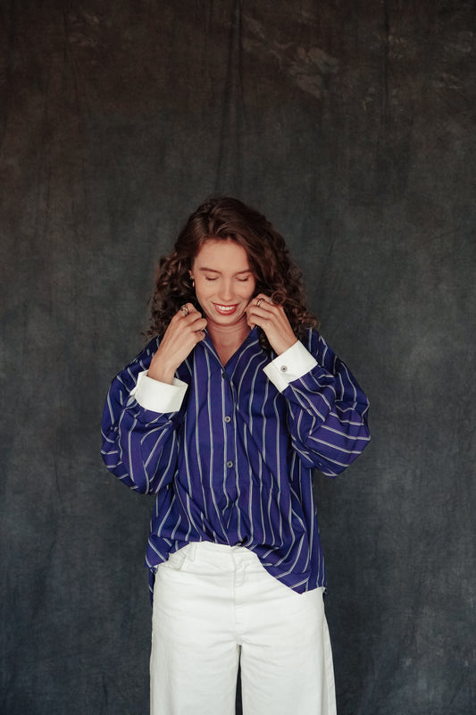 Person wearing a blue striped shirt and white pants against a dark background