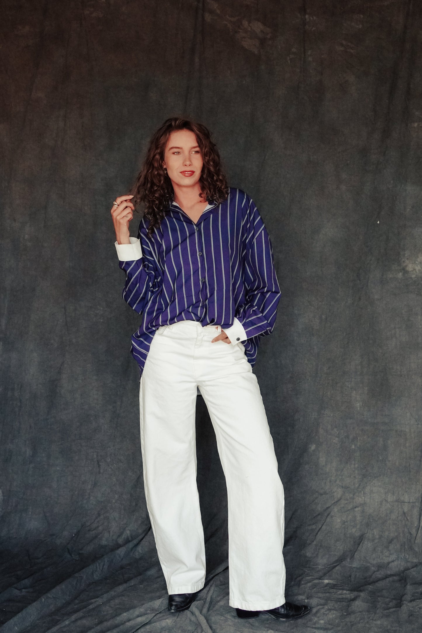Person wearing a striped shirt and white pants against a dark backdrop