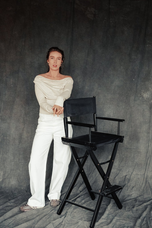 Person in white outfit standing next to a black chair against a gray background
