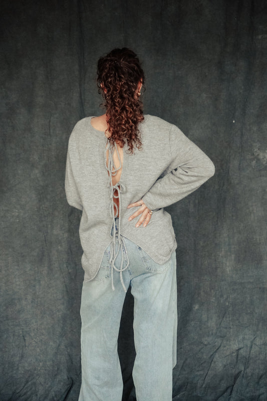 Person wearing a gray sweater and light blue jeans against a dark background.