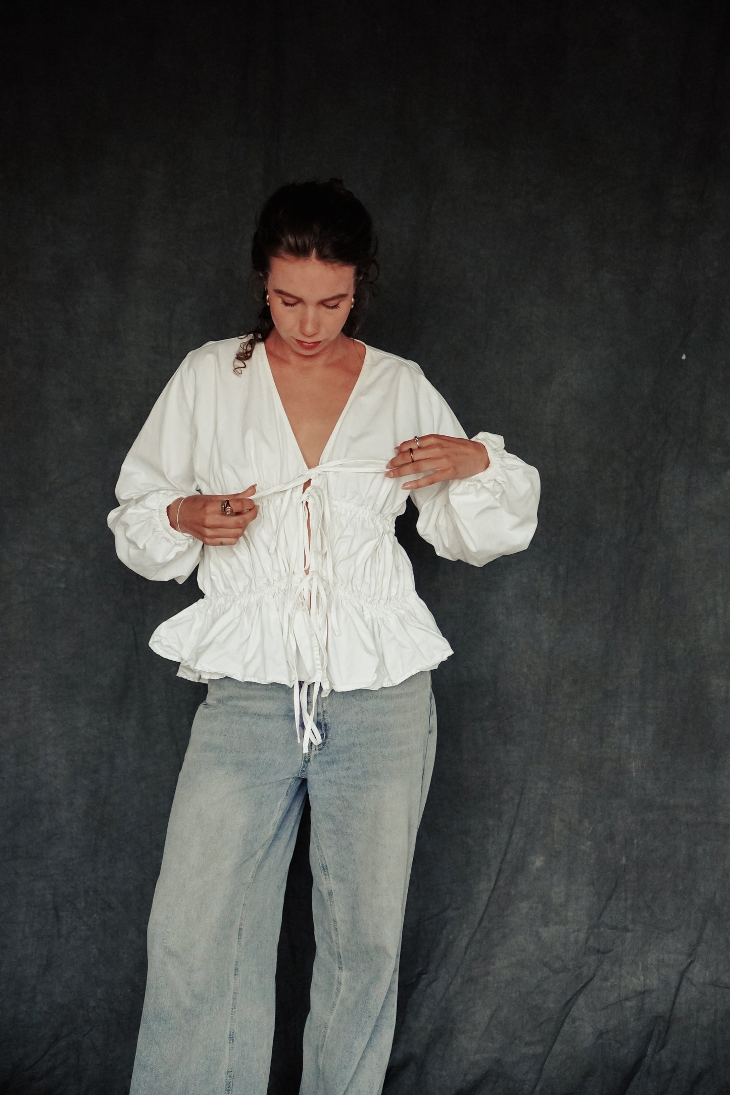 Person wearing a white blouse and light blue pants against a dark background