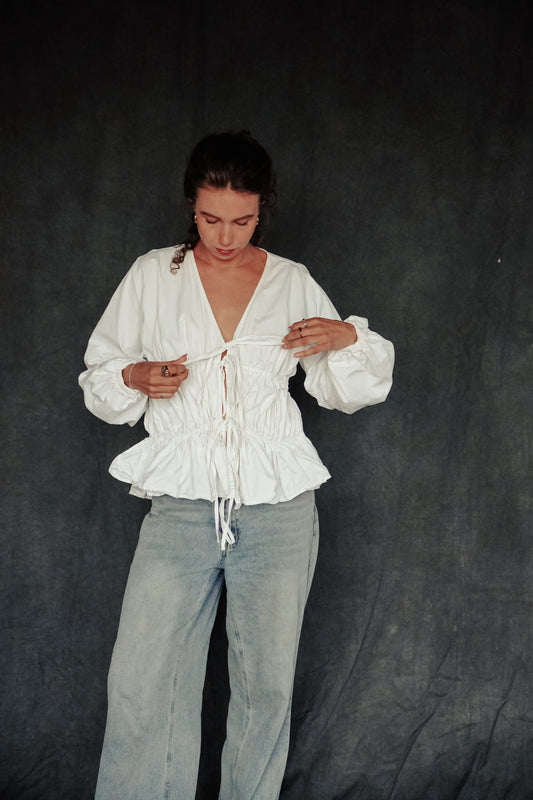 Person wearing a white blouse and light blue pants against a dark background