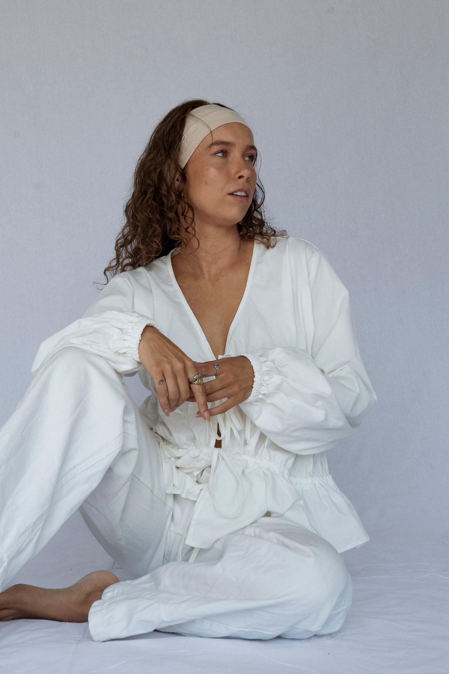 Woman wearing a white outfit sitting on a plain background