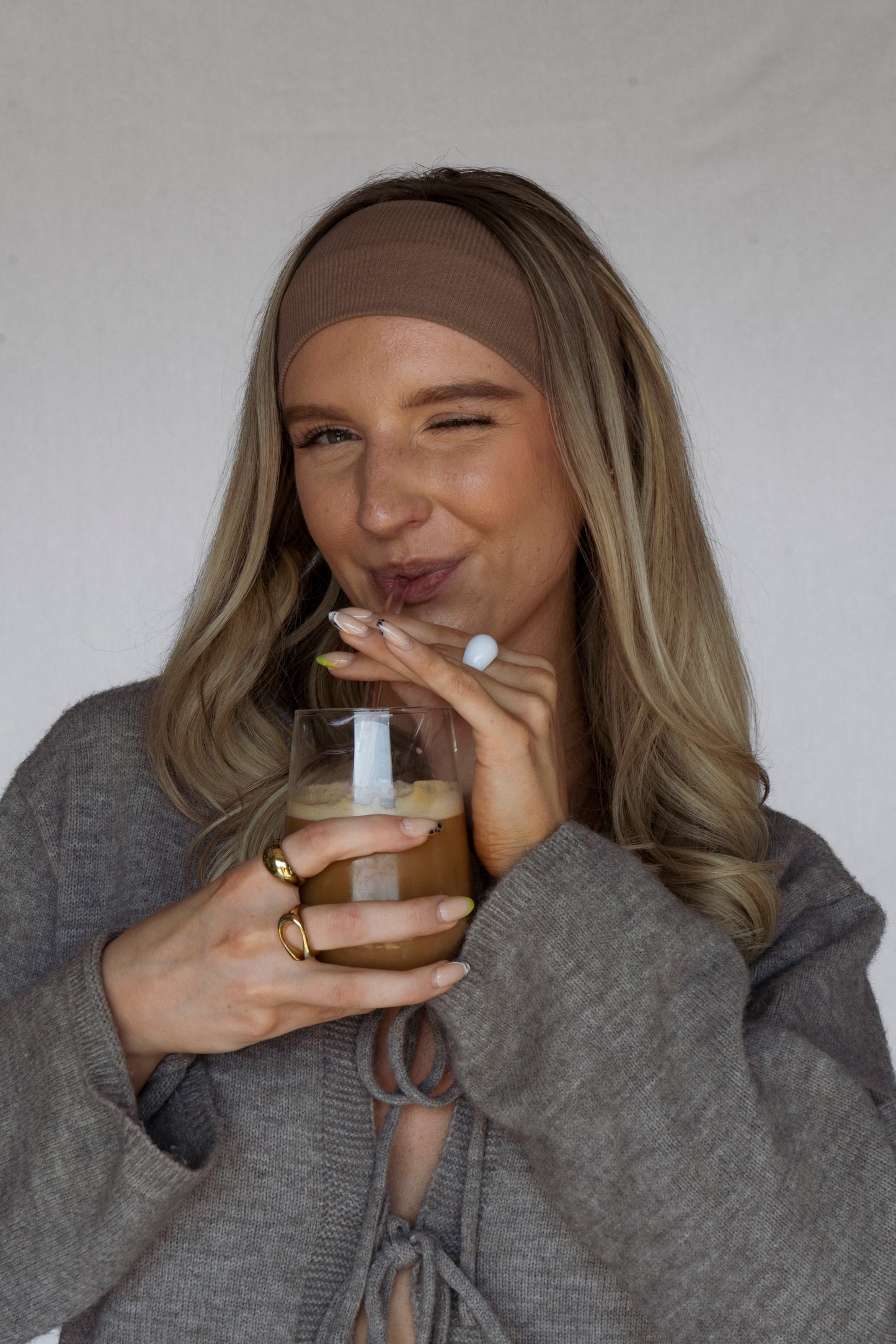 Woman drinking from a glass with a straw against a plain background
