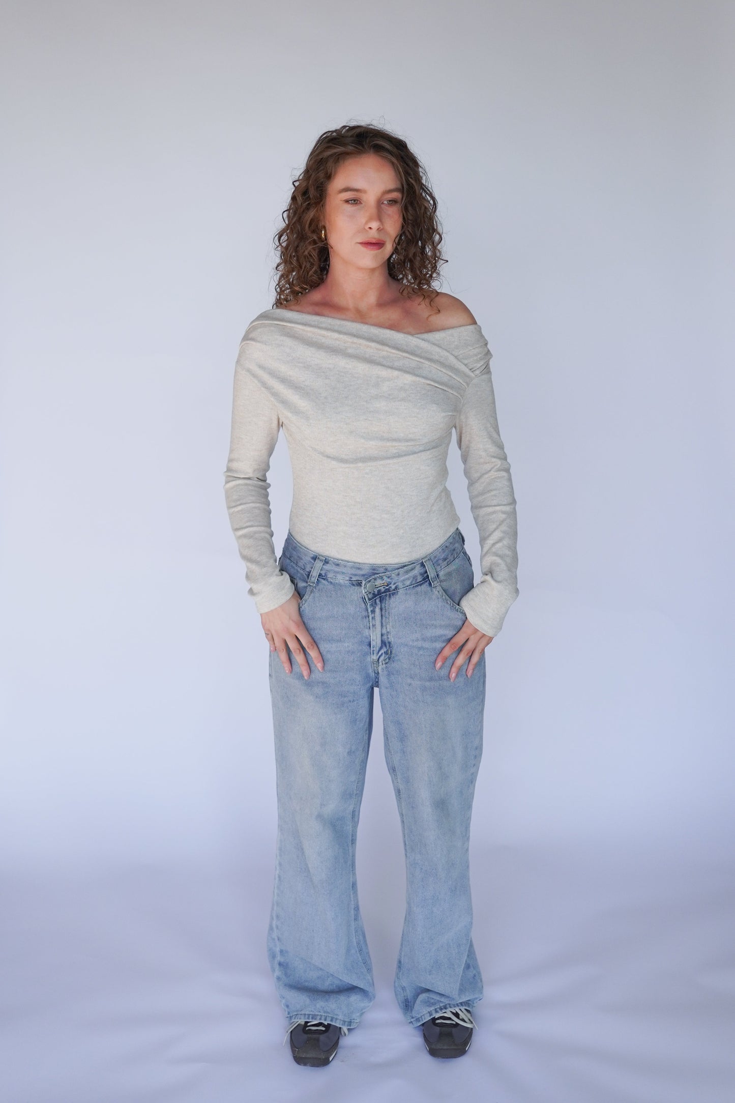 A person wearing light blue denim jeans and a beige off-the-shoulder top with long sleeves.