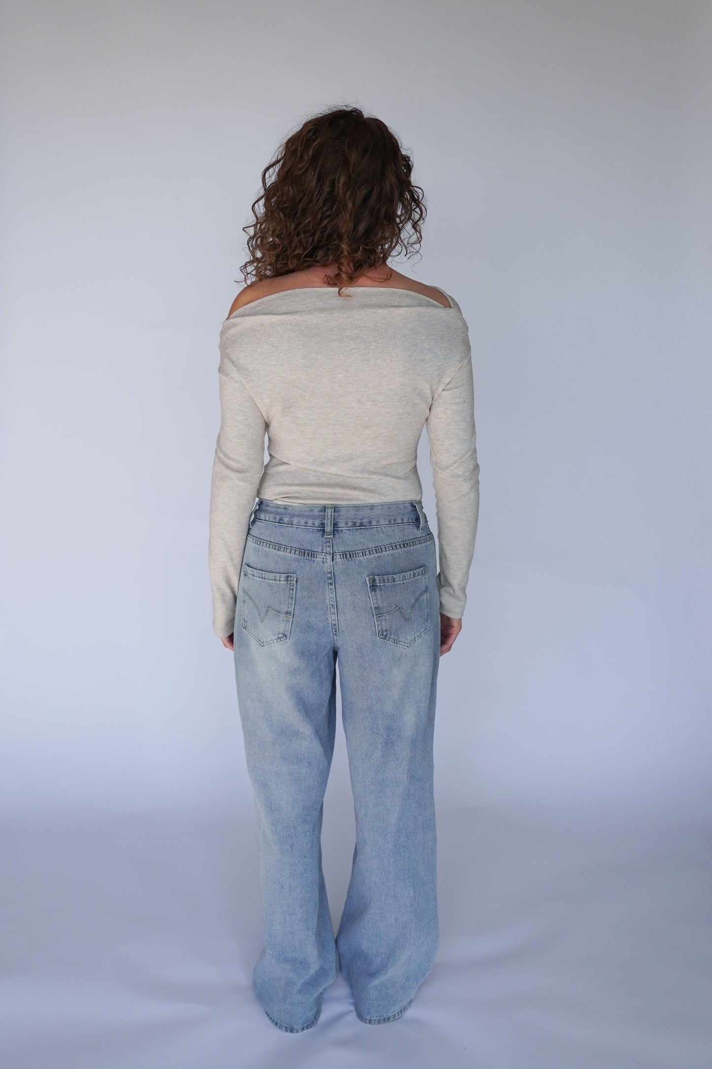 Person wearing light gray off-shoulder top and blue jeans on a white background