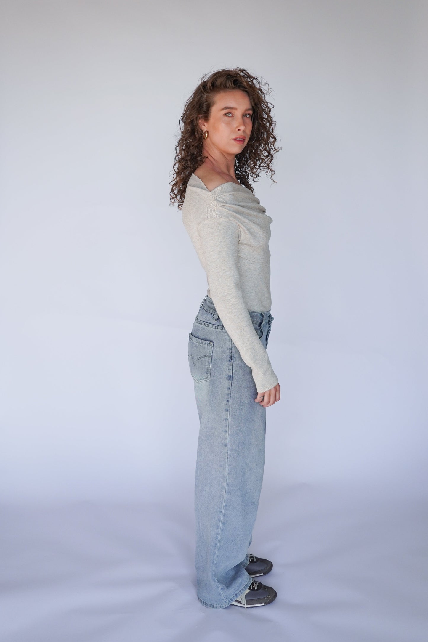 Person wearing a light gray sweater and blue jeans on a white background