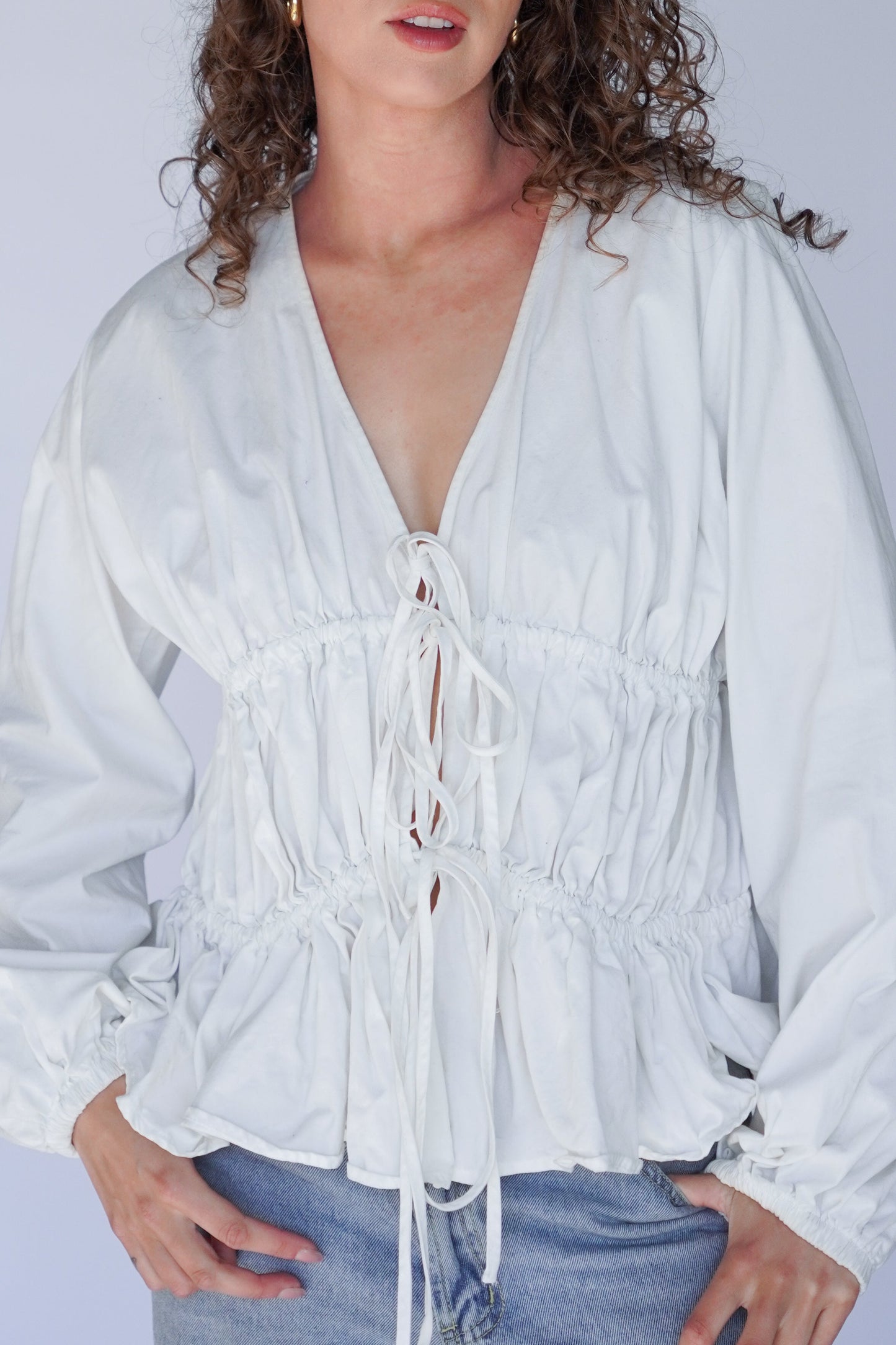 White blouse with lace-up front worn by a person against a plain background.
