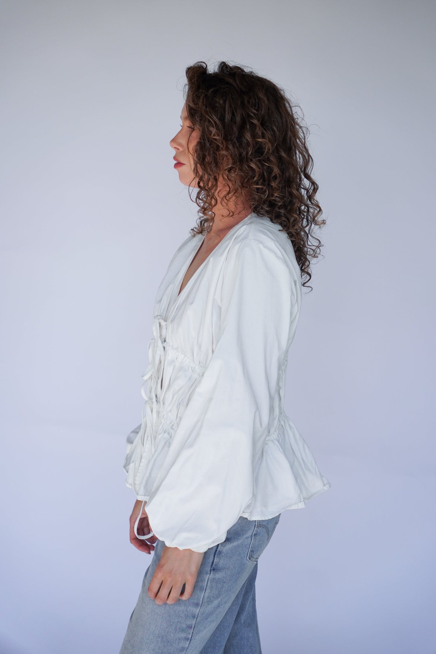 Person wearing a white blouse with ruffles, standing against a plain background.