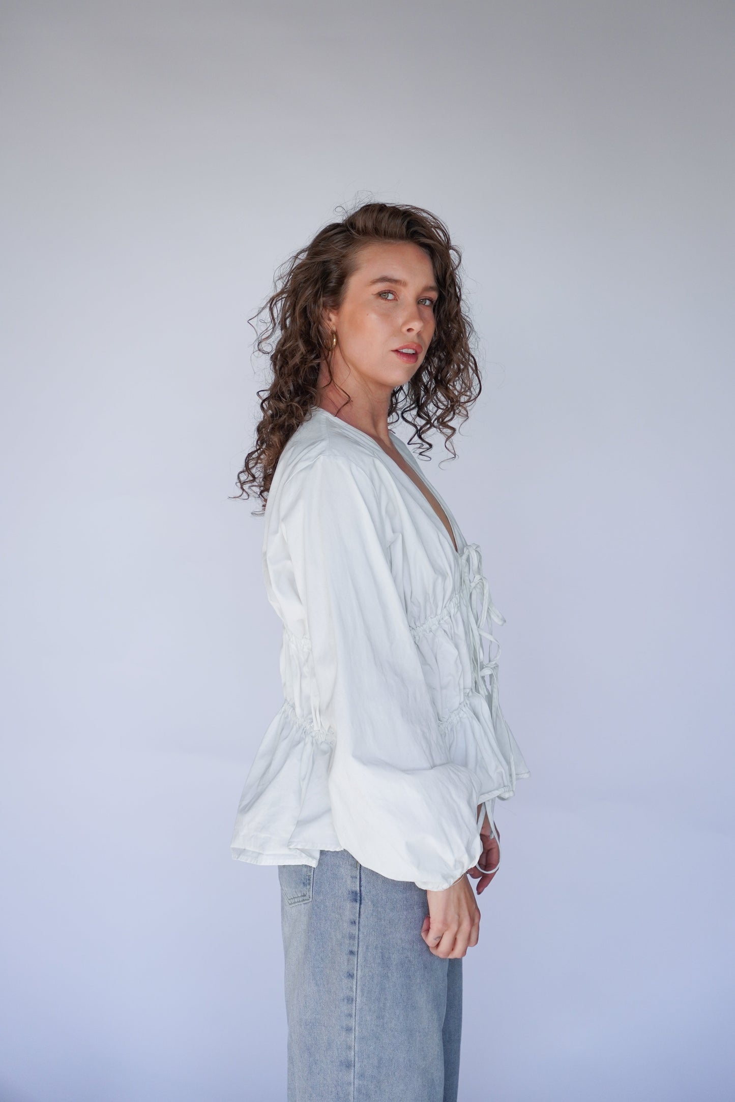 Woman wearing a white blouse and blue jeans against a plain background.