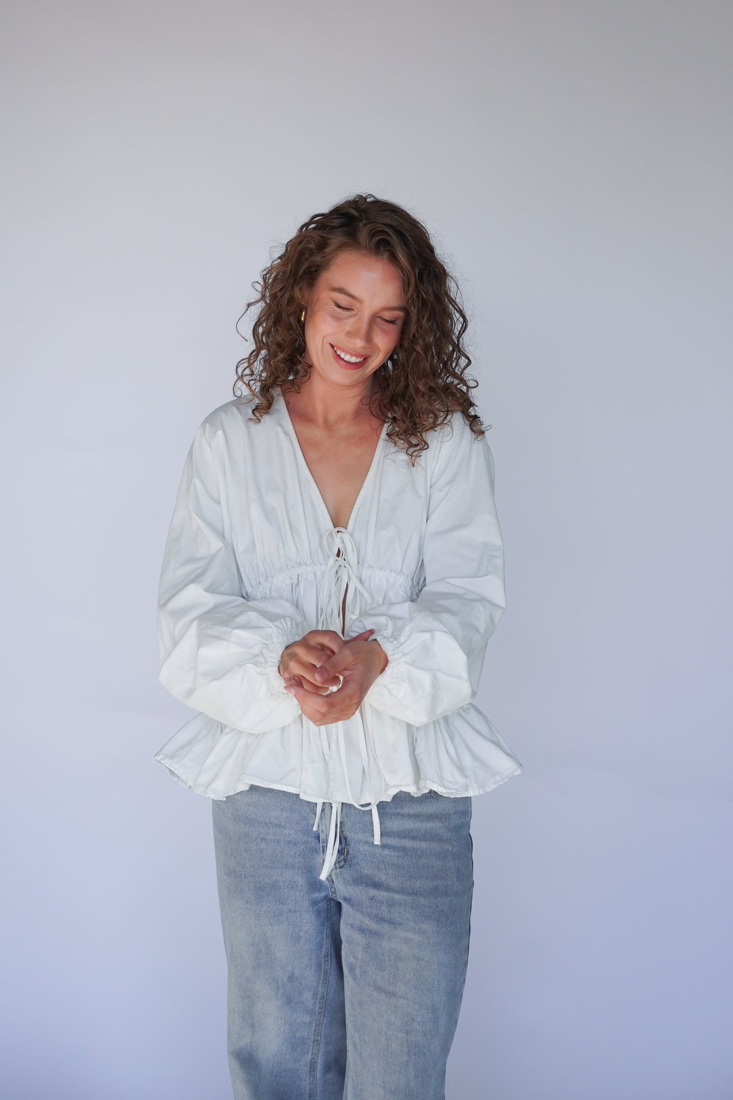 Woman in a white blouse and jeans against a plain background
