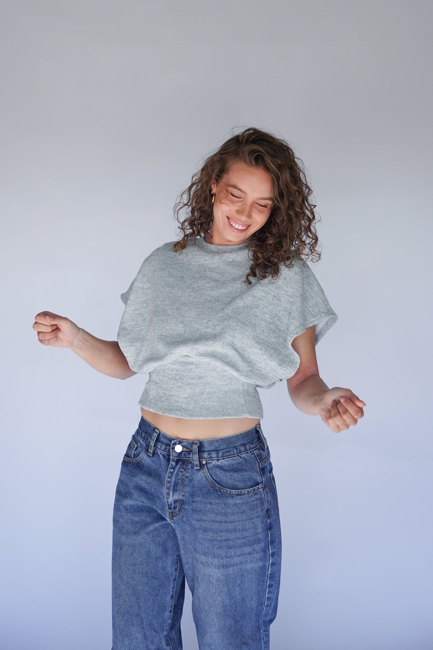 A person wearing a gray crop top with a built-in tank and jeans.