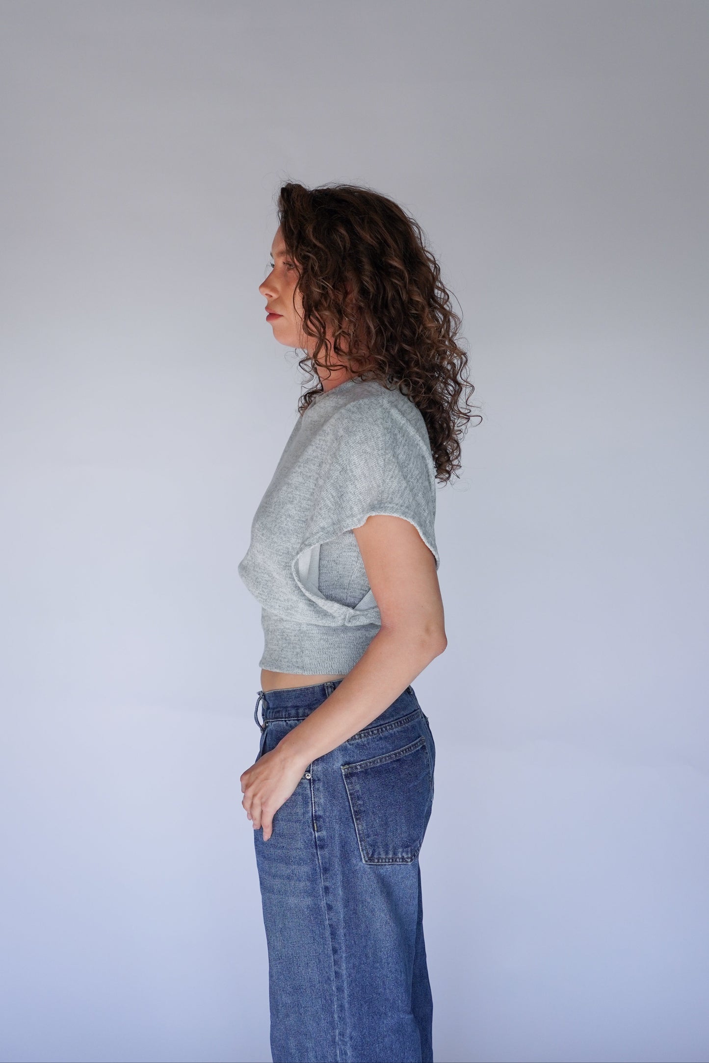 Person wearing a light gray crop top and blue jeans against a plain background.