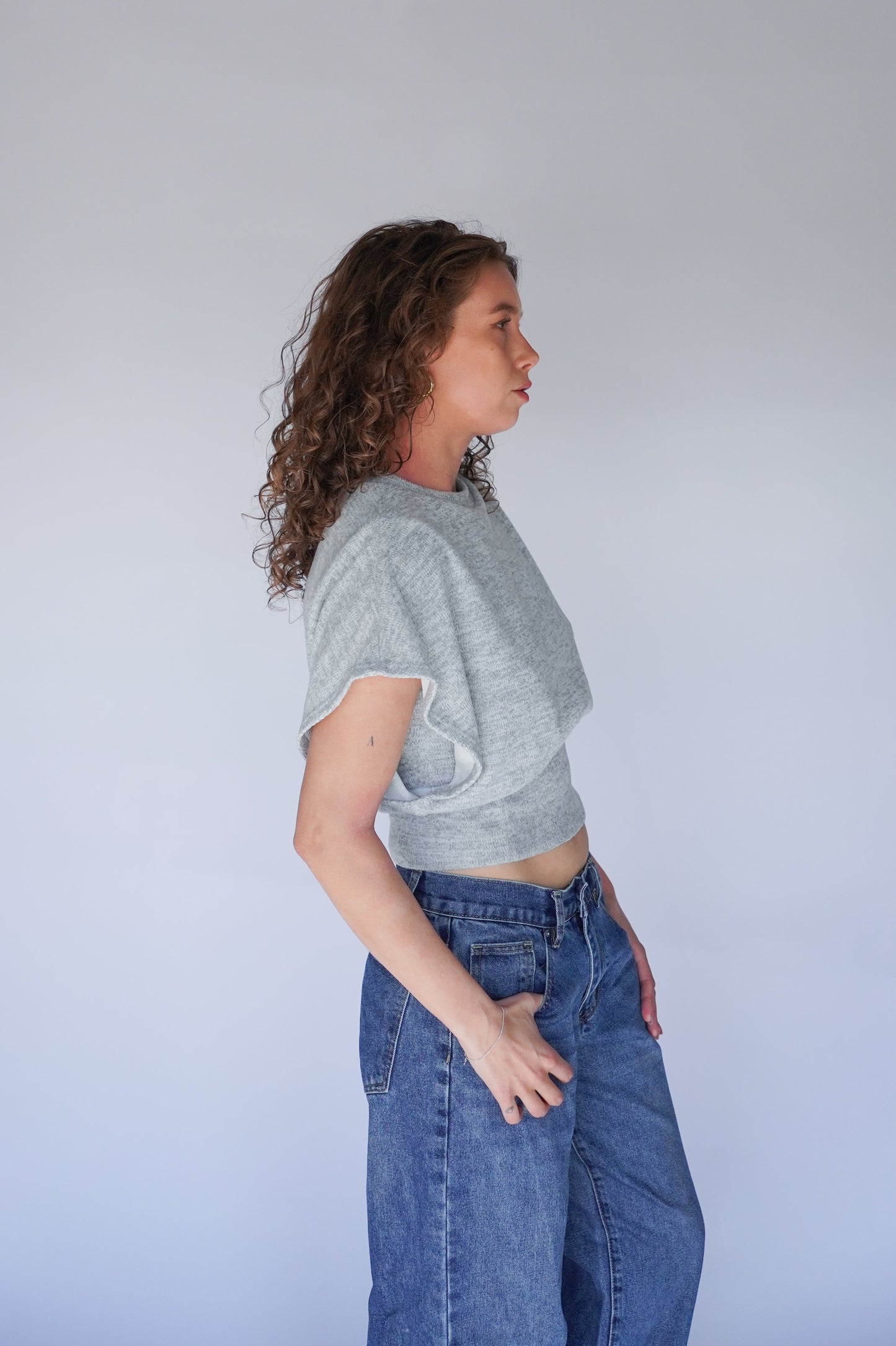 Person wearing a gray crop top and blue jeans against a plain background.