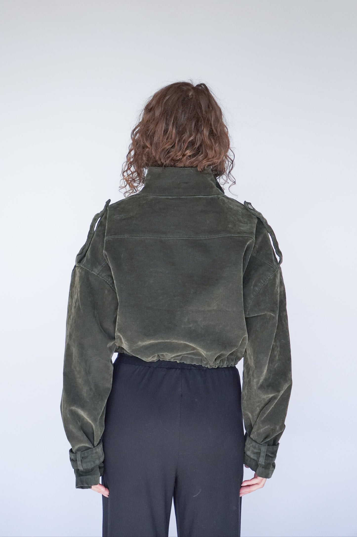 Person wearing a dark green jacket on a plain background