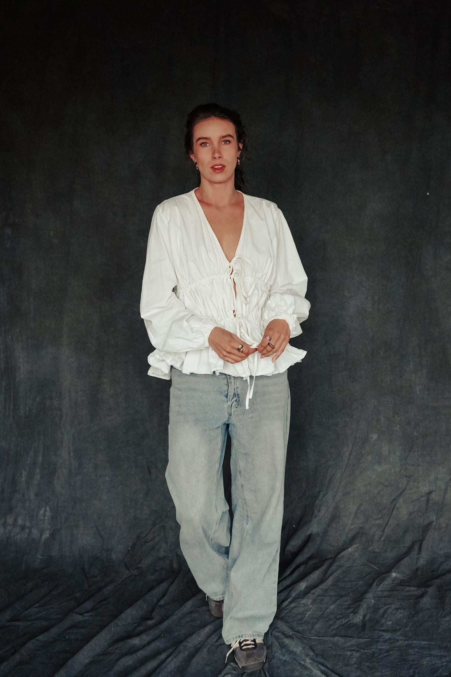 Person wearing a white shirt and light gray pants against a dark background