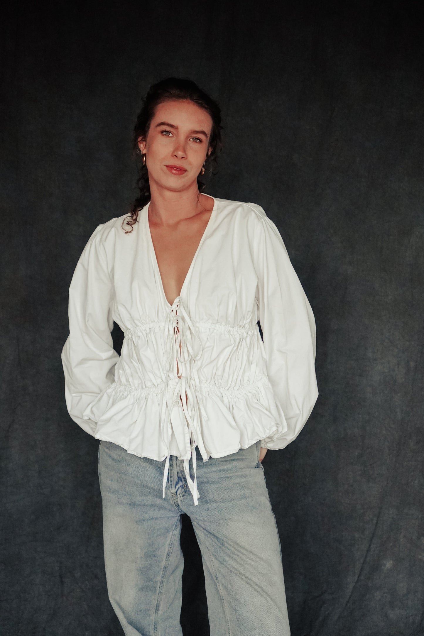 A person wearing a white Andie blouse with balloon sleeves and tie-front details, paired with blue jeans.